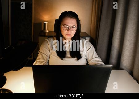 Woman working on computer late evening at home office. Concentrated female freelancer trying to solve business problems. Working and suffering from we Stock Photo