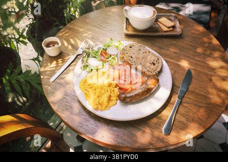 Scrambled eggs, fried pork sausage and sliced smoked salmon slices with rye bread toast and salad with radishes and Coffee with biscuits. A fresh brea Stock Photo