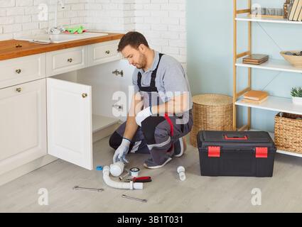 Man plumber in uniform with toolbox replacing the water filter or fixing broken pipe in kitchen. Stock Photo