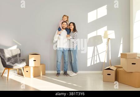 Excited family stands in their new home surrounded by moving boxes and is happy to move. Stock Photo