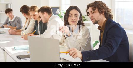 Young students collaborating in modern classroom, discussing project and analyzing data on laptop. Stock Photo