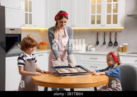 Mother and her kids with homemade cookies at wooden table in kitchen Stock Photo