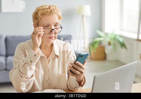 Serious focused woman, pensive lady using mobile phone for work at desk, communication, thinking Stock Photo