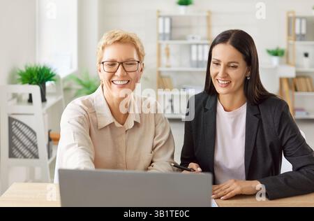 Cheerful female colleagues sitting at desk in office, collaborating on project and discussing ideas. Stock Photo