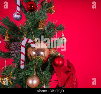 close up image of christmas tree decorations. Isolated red studio background. Red and white candy cane, gold colored balls, bells and red ribbon. Stock Photo