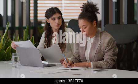 Multiethnic businesswomen two coworkers business partners multiracial girls African American Caucasian women colleagues working together documents Stock Photo