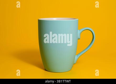 A single matte blue ceramic mug with a handle is placed against a solid yellow backdrop, minimal and clean studio lighting. Stock Photo
