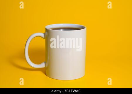 Upright white ceramic mug filled with dark coffee, placed on a vibrant yellow background in a minimalist studio setup. Stock Photo