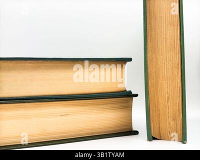 A stack of two old books with yellow tattered pages lying on top of each other and one book standing to the side of the stack on a white background, t Stock Photo