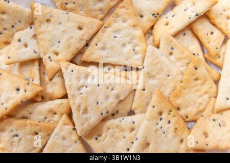 close up crispy triangular crackers top view. Dietary cereal with salt and poppy seed Stock Photo