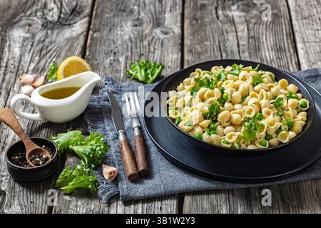 Pasta with green peas, pasta e piselli in black bowl on rustic wooden table with ingredients and fork, Italian recipe, horizontal view from above Stock Photo