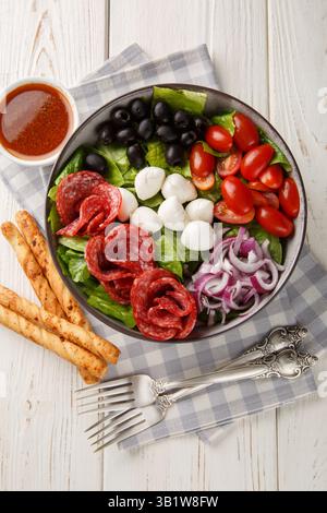 Crispy fresh bowl salad with salami sausages, cheese, tomatoes, olives, onions, romaine lettuce and spicy dressing served with breadsticks close-up on Stock Photo