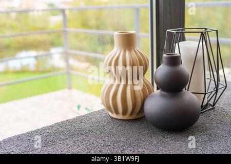 Two ceramic decorative vases or candlesticks in different shapes and colors are displayed on sleek table. Beautiful green landscape is visible through Stock Photo