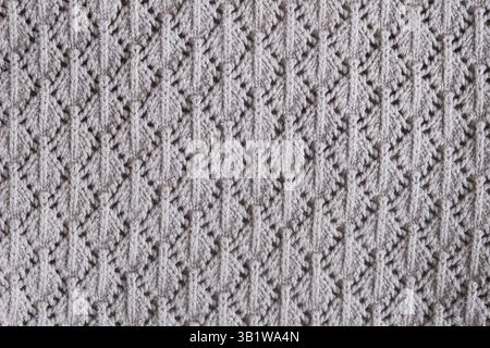 Knitted fabric with symmetrical lace pattern in light grey color. Close-up texture of handmade textile with repeating decorative stitches. Stock Photo