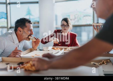 A diverse group of business employees share a pizza lunch in a bright office while discussing ideas and projects. Stock Photo