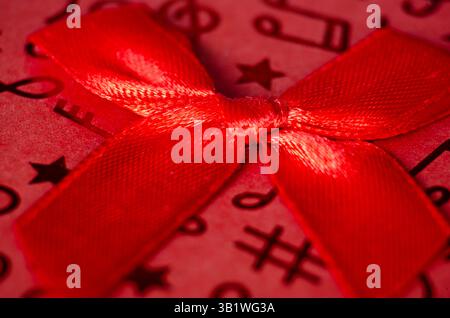Close up of red gift ribbon with white polka dots tied into a bow, placed on a textured red and pink striped background. Stock Photo