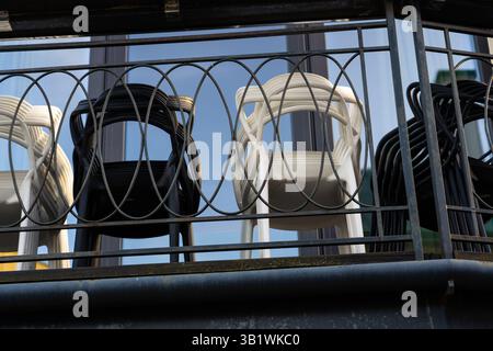 The plastic chairs are folded and stand on the balcony behind the fence Stock Photo