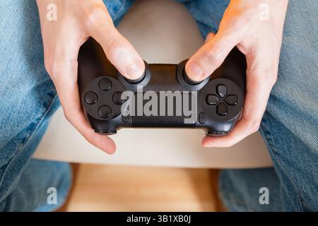Person holds a black video game controller with both thumbs on joysticks, ready to play, top view Stock Photo