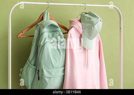 Rack with stylish pink hoodie, cap and backpack on green background Stock Photo