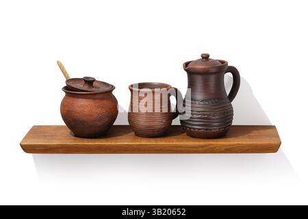 Clay jug with handle, pot and mug on oak wooden shelf isolated on white background, front angle view, design element Stock Photo