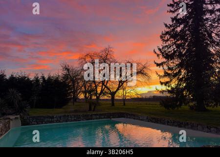 beautiful red cloudy sky sunset on countryside, swimming pool in foreground Stock Photo