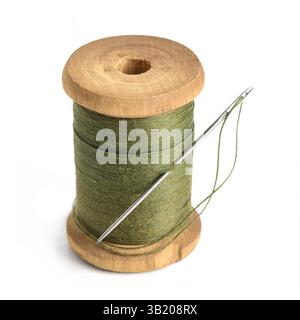 Old Single wooden spool of thread olive green color and needle Simple design of thread closeup white background Stock Photo