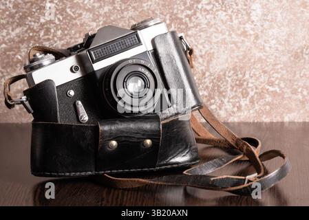 The Classic Vintage Old shabby Photo Camera in a dark brown case open lens brown natural leather Strap Wooden table Stock Photo