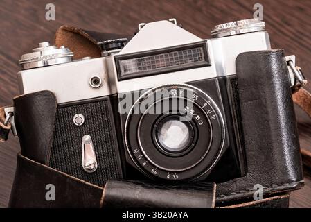 The Classic Vintage Old shabby Photo Camera in a dark brown case open lens brown natural leather Strap Wooden table Stock Photo
