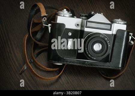 The Classic Vintage Old shabby Photo Camera in a black case open lens brown natural leather Strap on  Wooden table background Stock Photo