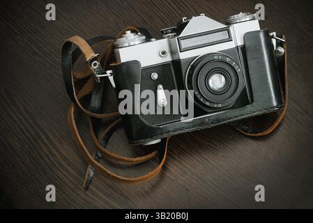 The Classic Vintage Old shabby Photo Camera in a black case open lens brown natural leather Strap on  Wooden table background Stock Photo