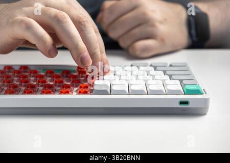 Close up view of hands placing white keycaps onto red low-profile switches on a white mechanical keyboard illustrating the process of tech assembly an Stock Photo