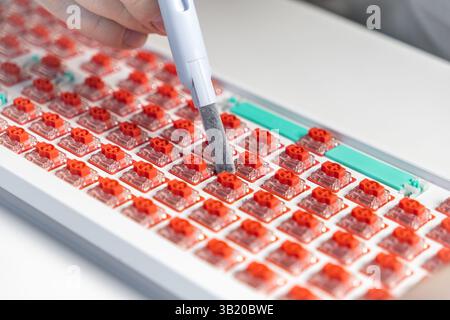Close-up of a red mechanical keyboard switch being cleaned with a handheld brush tool during assembly, highlighting custom mechanical keyboard mainten Stock Photo