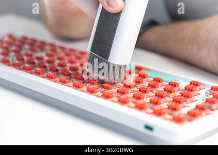 A hand operates a compact vacuum cleaner with soft bristles to clean red mechanical keyboard switches, focusing on PC hardware care, customization, an Stock Photo