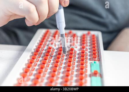 A hand uses a cleaning brush to remove dust and debris from a mechanical keyboard with red switches, focusing on maintenance and improving responsiven Stock Photo