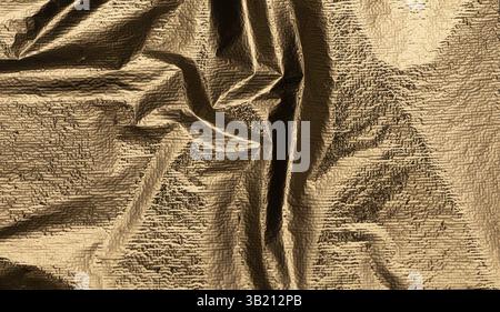 Crumpled brass and gold foil texture with a pearlescent finish, shining with a bright, elegant glow. Dark, rough folds and wrinkles create a luxurious Stock Photo
