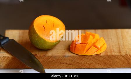Ripe mango being sliced into cubes on wooden board, knife beside mango, tropical fruit preparation. Stock Photo