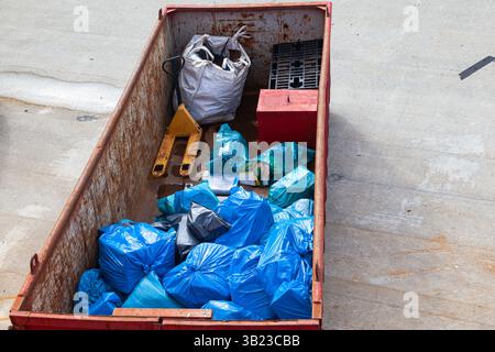 A large trash container with garbage bags inside and various construction debris. Stock Photo