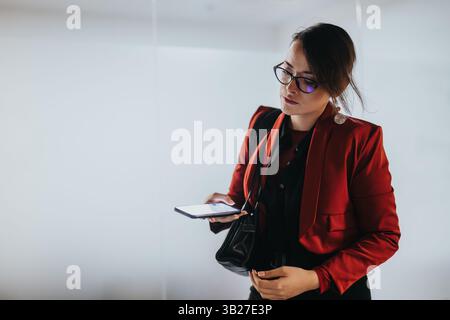 Businesswoman in a red jacket using smart phone at the office Stock Photo
