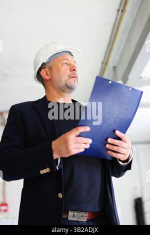 Businessman in hard hat standing on site, leading construction project with authority Stock Photo