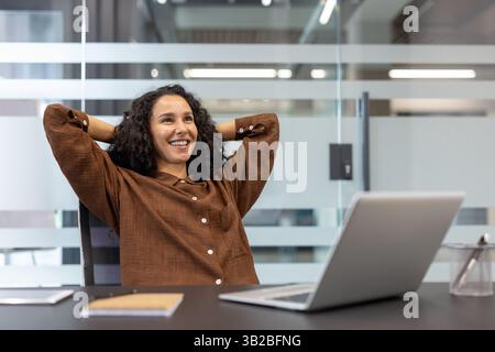 Successful businesswoman well done, successfully completed current project. Office worker with hands behind head resting and relaxing, enjoying results of achievement. Stock Photo
