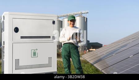 Farmer with digital tablet next to solar panels and energy storage. Farm using renewable energy.. Stock Photo