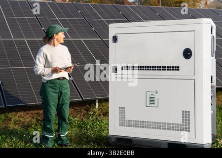 Farmer with digital tablet next to solar panels and energy storage. Farm using renewable energy.. Stock Photo