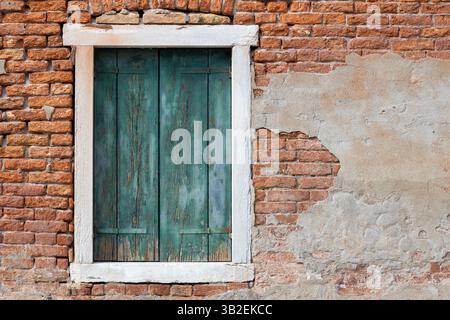 Aged green window shutters on rustic brick wall with peeling plaster Stock Photo