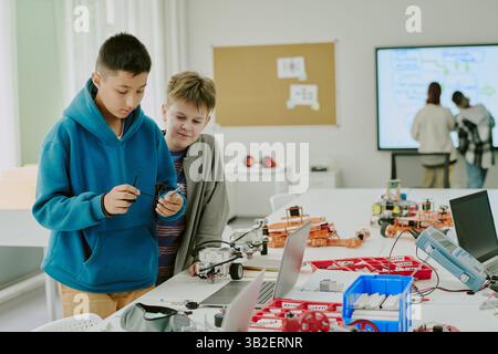 Best friends enjoying working on robot prototype in spacious classroom at school Stock Photo