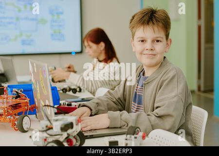 Medium close up portrait of boy looking at camera while using laptop at desk in classroom Stock Photo