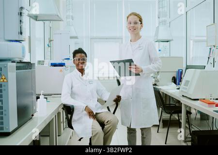 Scientists conducting groundbreaking research in high-tech laboratory, wearing lab coats and safety glasses while analyzing data and samples with advanced equipment Stock Photo