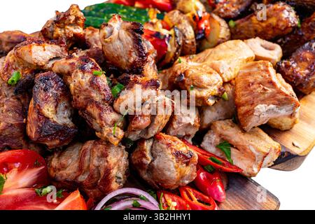 A vibrant arrangement of grilled meats served with fresh slices of tomatoes, onions, and peppers on a wooden board. The dish showcases a variety of fl Stock Photo