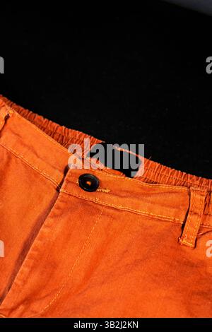 A neat image showing orange trousers with a button and elastic waistband on black background Stock Photo