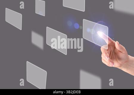 Fingertip interacting with transparent digital interface, displaying floating blank interactive screens against dark gray backdrop representing cuttin Stock Photo