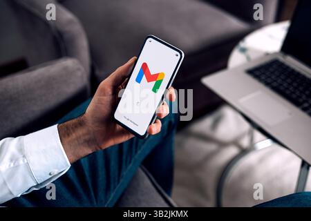 Business man in the office holding a mobile phone opening Gmail app for email of Google Workspace. ROSARIO, ARGENTINA - APRIL 22, 2025. Stock Photo